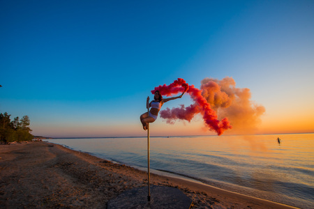 Athletic girl climbed on a portable pylon on the beach and holds a red smoke grenade. Sand, sunset, beach.の写真素材