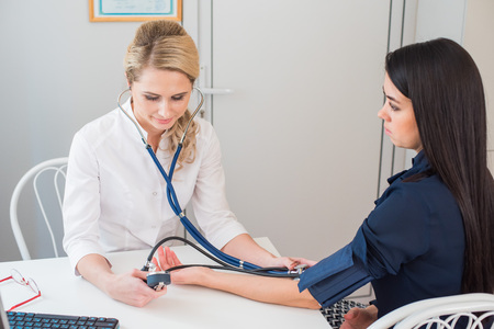 Doctor measuring pressure of the pregnant woman. Doctor taking blood pressure of female patient at officeの写真素材