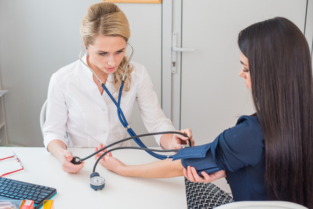Doctor measuring pressure of the pregnant woman. Doctor taking blood pressure of female patient at officeの写真素材