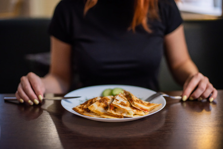 Woman eating delicious quesadilla in restaurant. Young redheaded woman is eating Mexican food in a cafeの写真素材