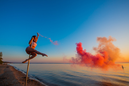 Athletic girl climbed on a portable pylon on the beach and holds a red smoke grenade. Sand, sunset, beach.の写真素材