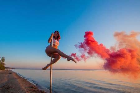 Athletic girl climbed on a portable pylon on the beach and holds a red smoke grenade. Sand, sunset, beach.の写真素材