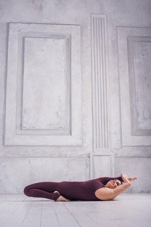 Woman meditating in a gym. Sporty young woman doing yoga practice on light background.の写真素材