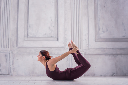 young sporty fit woman doing Ashtanga Vinyasa Yoga asana Dhanurasana - bow pose. Sporty young woman doing yoga practice on light background.の写真素材