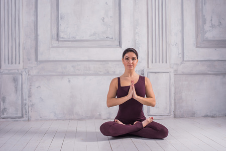 Sporty young woman doing yoga practice on light background, sitting in Lotus pose.の写真素材
