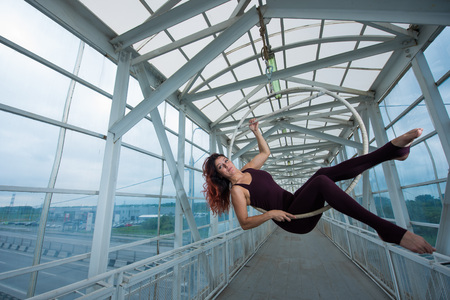 The red-haired aerial gymnast in a sports combo performs at the air hoop in a pedestrian crossing.の写真素材