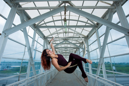 The red-haired aerial gymnast in a sports combo performs at the air hoop in a pedestrian crossing.の写真素材