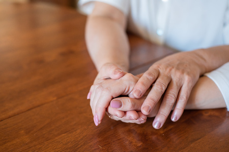 Elderly mother and her daughter holding hands while sitting at the table.Close up on women of different generations holding hands. Close Up Shot Of Mother And Daughter's Hands Holding.の写真素材