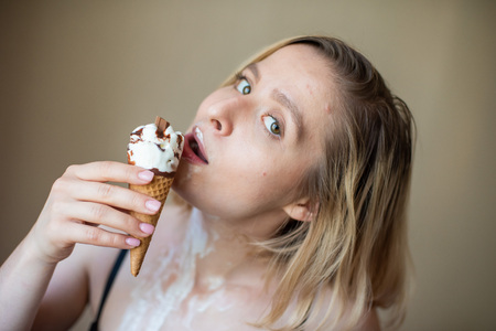 Sexy blonde licks a waffle cone. Ice cream is melting, erotically draining through the body of an attractive woman. Beautiful girl smeared with ice creamの写真素材