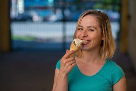 Portrait of a cute girl in a green dress is walking outside and eating dessert. Beautiful blonde enjoying a cone with ice cream on a beautiful summer day. Life is a pleasure.の写真素材