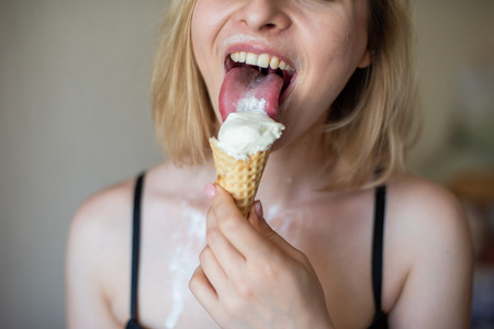 Sexy blonde licks a waffle cone. Ice cream is melting, erotically draining through the body of an attractive woman. Beautiful girl in black underwear smeared with ice cream. Close-up.の写真素材
