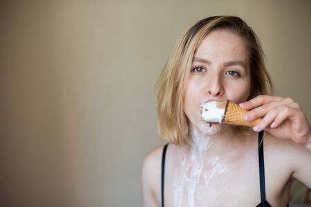 Sexy blonde licks a waffle cone. Ice cream is melting, erotically draining through the body of an attractive woman. Beautiful girl smeared with ice creamの写真素材