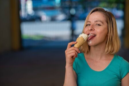 Portrait of a cute girl in a green dress is walking outside and eating dessert. Beautiful blonde...