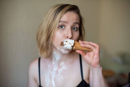 Sexy blonde licks a waffle cone. Ice cream is melting, erotically draining through the body of an attractive woman. Beautiful girl smeared with ice creamの写真素材