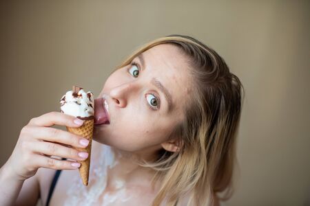 Sexy blonde licks a waffle cone. Ice cream is melting, erotically draining through the body of an attractive woman. Beautiful girl smeared with ice creamの写真素材
