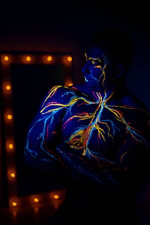 UV patterns body art of the circulatory system on a man's body. On the torso of a muscular athlete, veins and arteries are drawn with fluorescent dyes. Bodybuilder standing by the mirror with lampsの写真素材