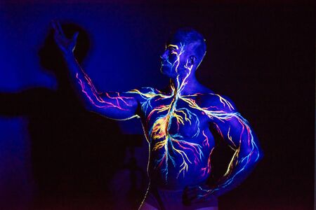 UV patterns body art of the circulatory system on a man's body. On the chest of a muscular athlete, veins and arteries are drawn with fluorescent dyes. The bodybuilder straightened the biceps.の写真素材
