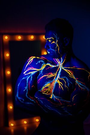 UV patterns body art of the circulatory system on a man's body. On the torso of a muscular athlete, veins and arteries are drawn with fluorescent dyes. Bodybuilder standing by the mirror with lampsの写真素材