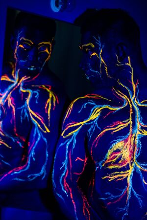 UV patterns body art of the circulatory system on a man's body. On the chest of a muscular athlete, veins and arteries are drawn with fluorescent dyes. Bodybuilder is standing at the mirrorの写真素材