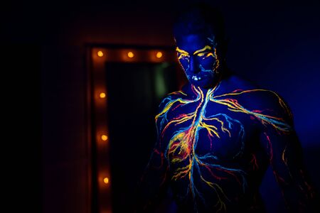 UV patterns body art of the circulatory system on a man's body. On the torso of a muscular athlete, veins and arteries are drawn with fluorescent dyes. Bodybuilder standing by the mirror with lampsの写真素材