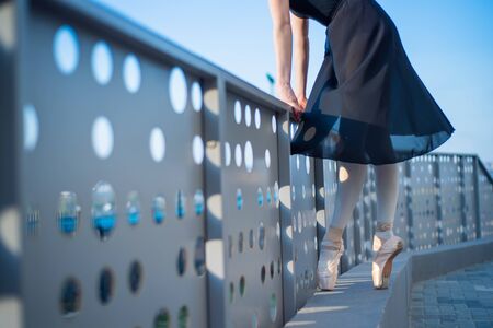 Ballerina in ballet legs in shoes and black tutu dancing by the fence. Beautiful young woman in...