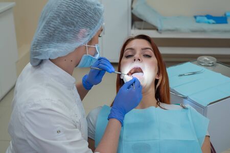 Woman dentist checking her patient for caries. Red-haired woman examined by a doctor. The girl will do the health of the teethの写真素材