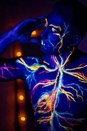 UV patterns body art of the circulatory system on a man's body. On the torso of a muscular athlete, veins and arteries are drawn with fluorescent dyes. Bodybuilder standing by the mirror with lampsの写真素材