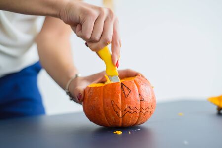 A woman carves her face on a pumpkin for a Halloween lamp on a black table. Close-up female hands making Jack-o'-lantern to the eve of all saints.