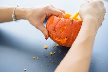 A woman carves her face on a pumpkin for a Halloween lamp on a black table. Close-up female hands making Jack-o'-lantern to the eve of all saints.の写真素材