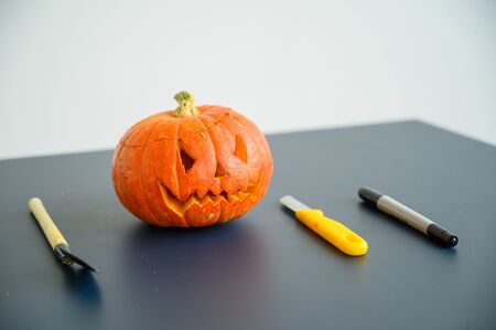 Little pumpkin with spiteful grimass, paper knife, pen, trowel over black background. Halloween concept, flat lay, top view. The process of making jack-o-lantern. flat layの写真素材