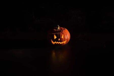 Halloween, orange pumpkin with a scary luminous face on a dark background. Thick gray smoke comes out and spreads across the black table. A close-up of a flashlight. Decorated candle stand.の写真素材