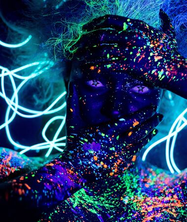Body art and contact lenses glowing in ultraviolet light. Portrait of a woman painted in fluorescent powder. Stars in the eyes. Neon light ribbon.の写真素材