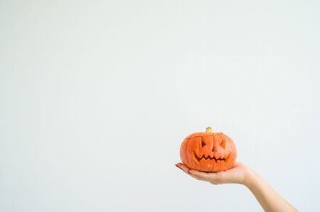 Female hand holding a pumpkin for Halloween. Close-up jack-o-lantern cover on a white background on the eve of all the saints. front view. Hand made for the holiday. Trick or treat.の写真素材
