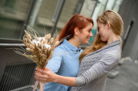 Same-sex relationships. Happy lesbian couple with dried flowers. Two beautiful women tenderly hug each other on a date. Bouquet in the foreground. Close up to couple hands.LGBT.の写真素材
