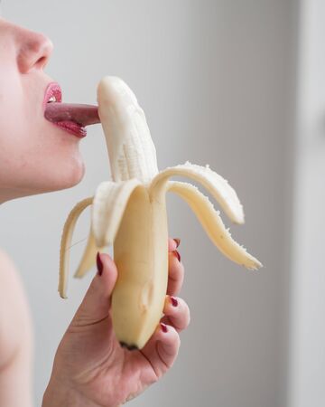 Close-up of the face, lips, tongue of a young, European girl licking a big yellow, sweet banana.の写真素材
