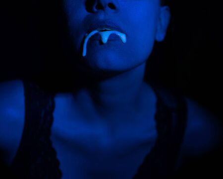 A thick white liquid flows down the lips of a young European girl. Dripping down. Ultraviolet, blue light. Close-up portrait. Spit out.の写真素材