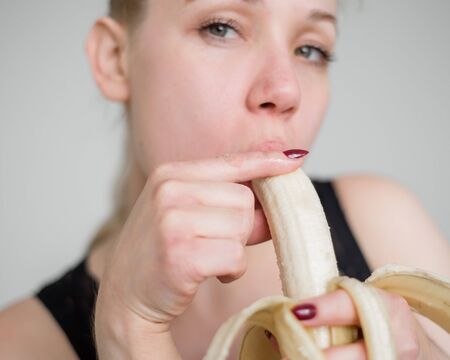 Close-up of the face, lips, tongue of a young, European girl licking a big yellow, sweet banana.の写真素材