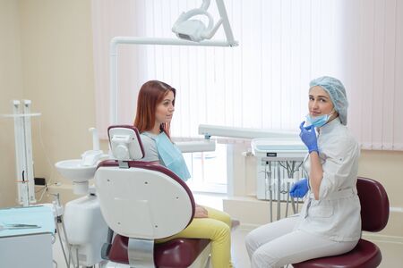 A female dentist and a red-haired patient in an office after dental treatment are looking at the camera with happy faces. Happy woman with her doctor after taking shows. Dental services.の写真素材