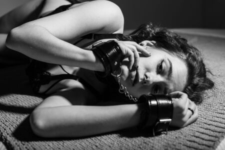 A young girl in sexy lingerie, lying on the bed handcuffed. BDSM games and entertainment. Sexual perversion.の写真素材