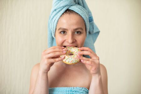 The girl in a towel has breakfast in the bed. A young attractive woman eats donuts in bed. The girl...