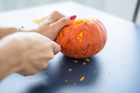 A woman carves face on a pumpkin for a Halloween lamp on a black table. Close-up female hands making Jack-o-lantern to the eve of all saints..の写真素材