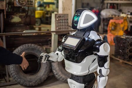 Humanoid robot on wheels with a monitor on his chest, shaking hands with a man. The old cluttered garage.の写真素材