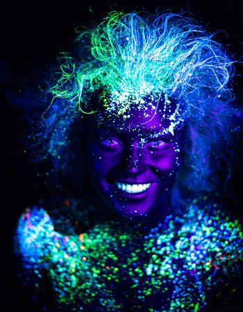 Body art and contact lenses glowing in ultraviolet light. Woman smiling, painted in fluorescent powder. Stars in the eyesの写真素材