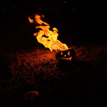 Tongues of flame in a pumpkin. jack-o-lantern on fire on a black background. Halloween symbol on the ground. Trick or treat. Close up.の写真素材