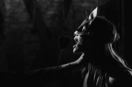 A man in a shirt holds a submissive lover by the neck. A woman in a leather cat mask bites a leather whip. BDSM Games for adults. Sensual lips. Black and white.の写真素材