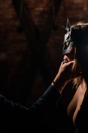 A man in a shirt holds his fingers on the sensual lips of a submissive lover. Portrait Woman in a leather cat mask. BDSM Games for adults.の写真素材
