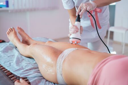 Woman receives an electric massage against cellulite. The doctor performs ultrasonic cavitation...