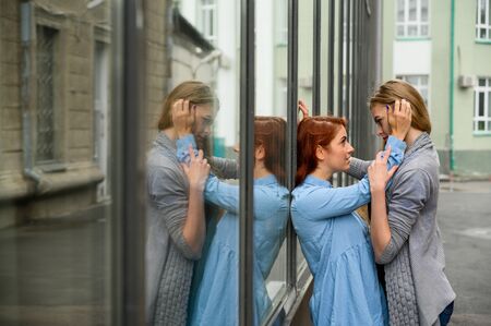 Portrait of two lesbians standing on the street and gently touching each other. LGBT Young loving female gay couple. The girl passionately presses her life partner against the mirror wall.の写真素材