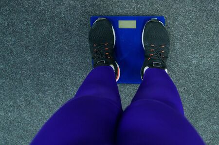 Fat woman is weighed in the gym. Top view on female legs in sneakers on electronic scales. Obesity.の写真素材
