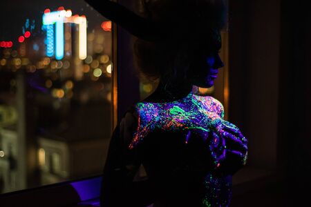 Woman in multi-colored drops of ultra-violet paint with Neon String Lights. Fluorescent body art. UV...